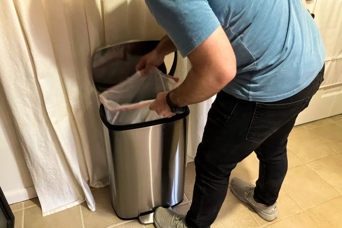 A person inserting a garbage bag into the Amazon Basics 13.2 Gallon Soft-Close Trash Can with Foot Pedal