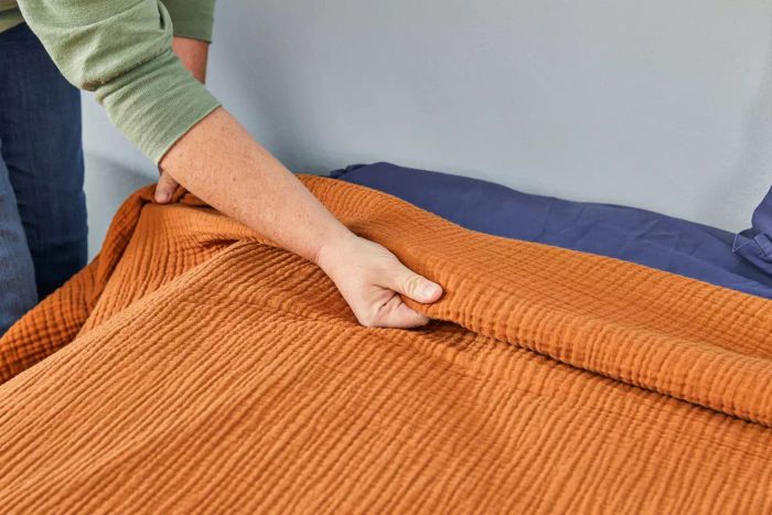 A close-up shot of someone adjusting the bed with the Quince Organic Airy Gauze Blanket