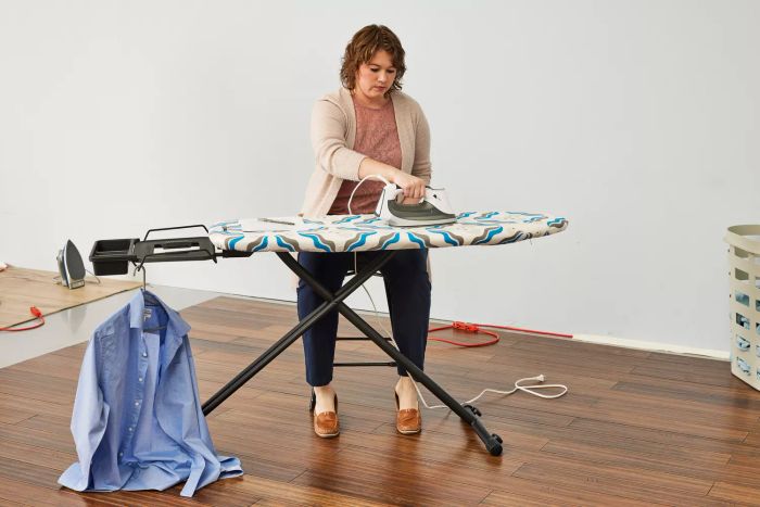 A t-shirt draped over the ironMATIK Space Maker Premium Ironing Board while a person presses an iron onto the surface.