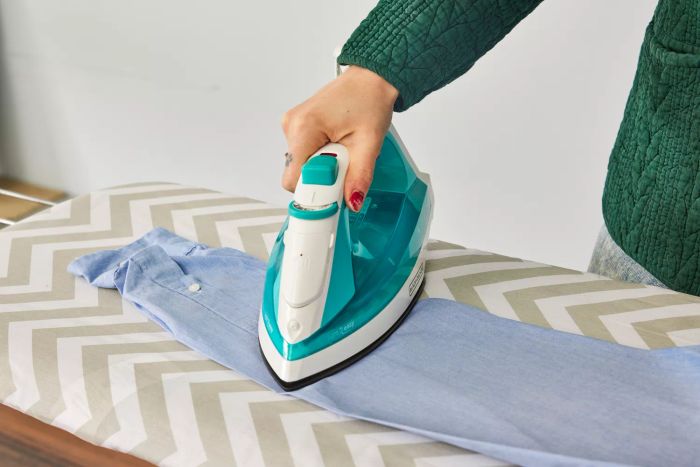 A close-up shot of a hand pressing an iron onto clothes on the Amazon Basics Full-Size Ironing Board, demonstrating its use.