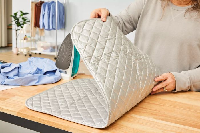 A person unrolling the BNYD Portable Ironing Mat Blanket on a wooden table