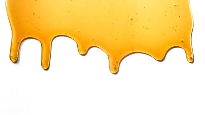A close-up shot of golden honey drips on a clean white surface, showcasing its sweet texture.