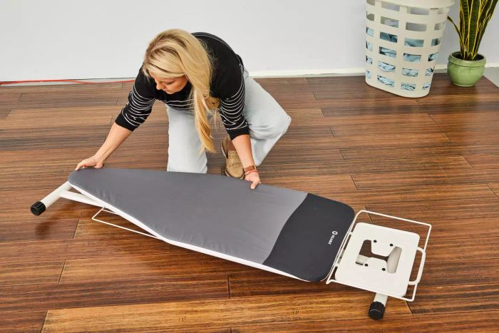 A person placing the Reliable 320LB Home Ironing Board on a wooden floor
