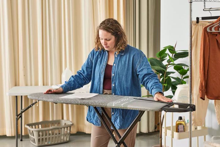 A person pressing down on the Bartnelli Heavy Duty Ironing Board while reading a newspaper.