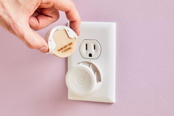 A hand inserting a fragrance cartridge into the Enviroscent Plug Hub, which is connected to a wall socket