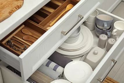 Open the kitchen cabinet drawers to reveal an assortment of dishware.