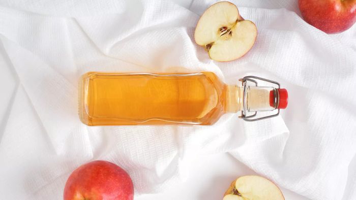 A Bottle of Apple Cider Vinegar Surrounded by Fresh Apples on White Fabric