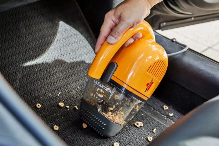 A person using a handheld vacuum to clean up spilled food in a car