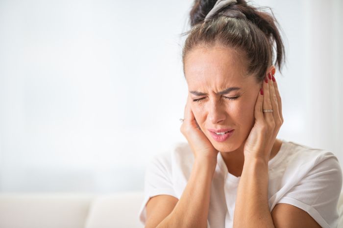 A woman with her eyes shut and her hands covering her ears