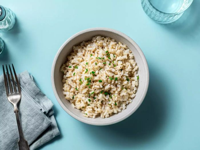 overhead view of a bowl of rice with a napkin, fork and glass on a teal surface