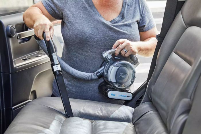 A person using a handheld vacuum to clean a car seat