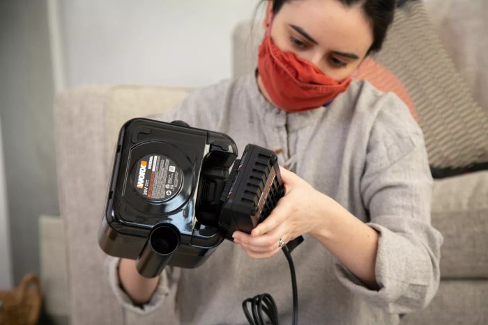 A woman attaching a battery pack to the WORX WX030L 20V Power Share Cordless Cube Vac Compact Vacuum