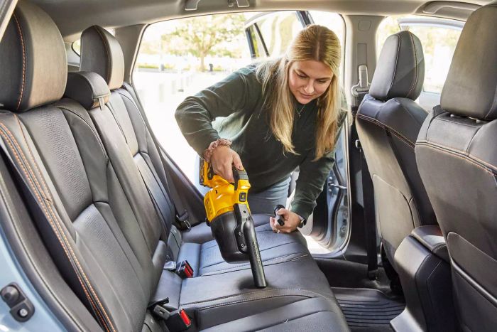 A woman using the Dewalt 20-Volt Cordless Handheld Vacuum to clean dust from car seats