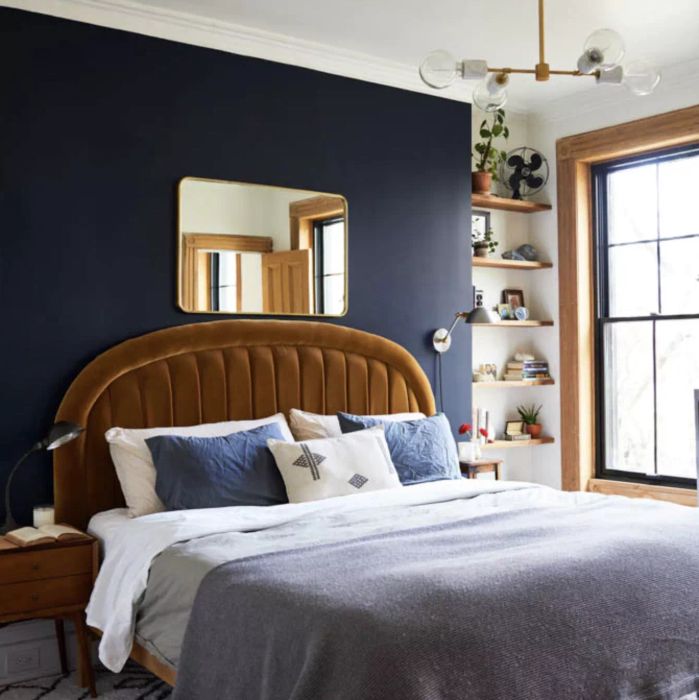 A navy-painted bedroom featuring a mustard velvet headboard and a window