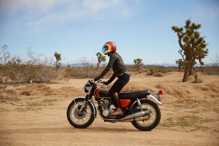 A lone rider, dressed in black with a red helmet, speeds across a vast desert landscape on a red motorcycle.