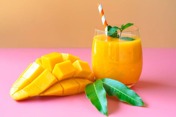 Mango smoothies topped with a mint leaf, set against a vibrant orange and pink background, perfect for a refreshing summer drink.
