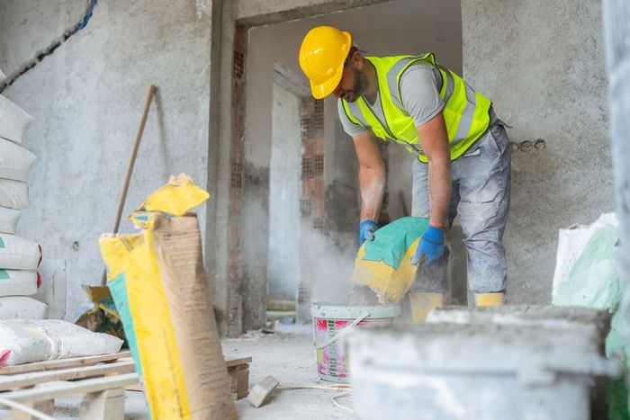 A construction worker prepares cement by mixing it to form concrete at a building site.