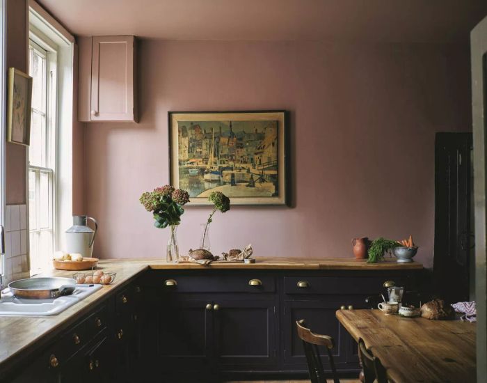 A kitchen featuring lower cabinets in Paean Black and walls in a rose-pink shade called Sulking Room Pink. Wooden counters are adorned with floral decorations.