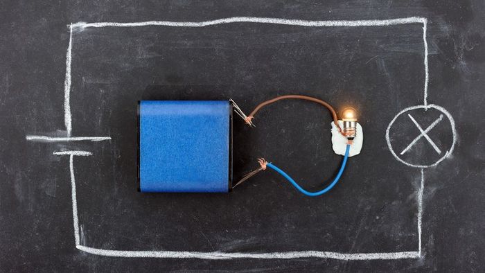 A blackboard displays a DC circuit featuring a battery and a light bulb, complete with a schematic diagram.