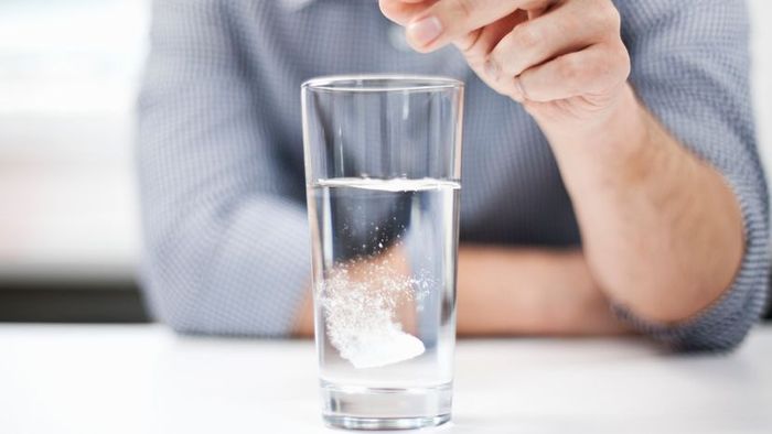 A person placing a dissolvable tablet into a glass of water.