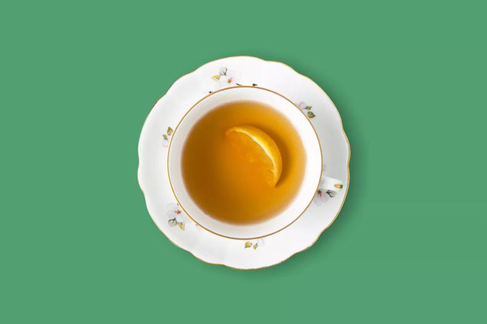 A steaming cup of tea featuring a fresh lemon slice, set against a vibrant green background with ample space for text.
