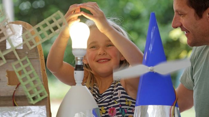 A young girl places her hand above a glowing light bulb, sharing a joyful moment with her father.