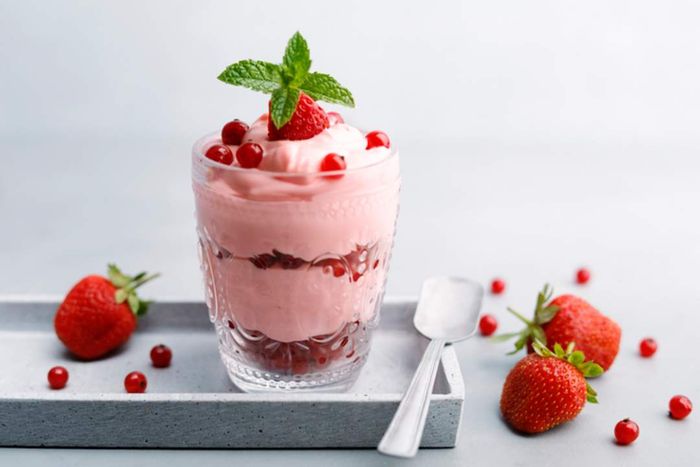 A layered dessert featuring pink strawberry cream and fresh strawberries, elegantly presented in a glass on a tray with a spoon.