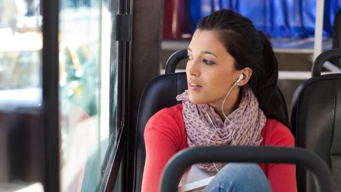 A woman in India listens to music on a bus, wearing headphones.