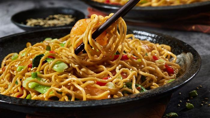 A black bowl of Asian-style noodles accompanied by vegetables