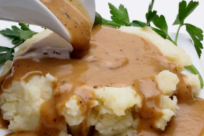 A plate of mashed potatoes, topped with rich, flowing gravy.