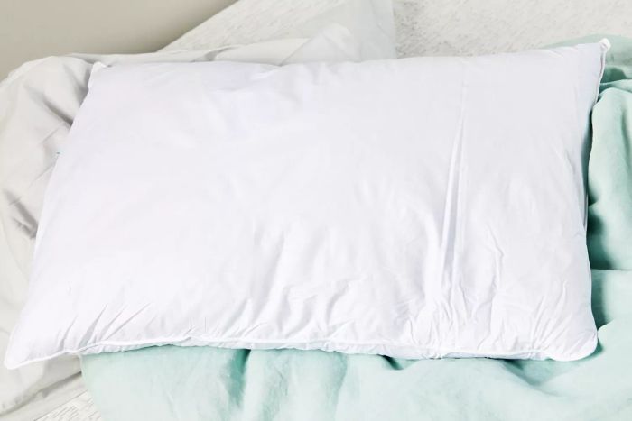 The Puredown Feathers Blend Pillow displayed on a light blue comforter