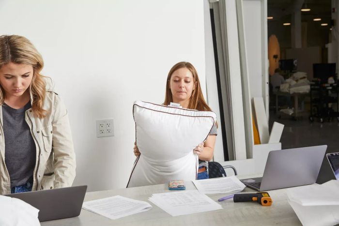 A person holding a Saatva Latex Pillow while standing in front of a table