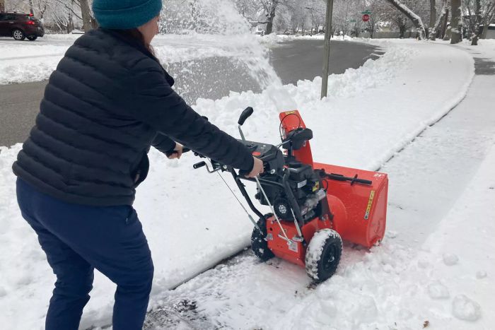 A person is seen clearing snow from a sidewalk using the Ariens Classic 2-Stage 24-Inch Snow Blower.