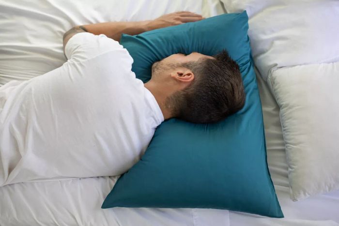 A man sleeping on Coop Sleep Goods The Original Pillow with a blue pillowcase on a bed