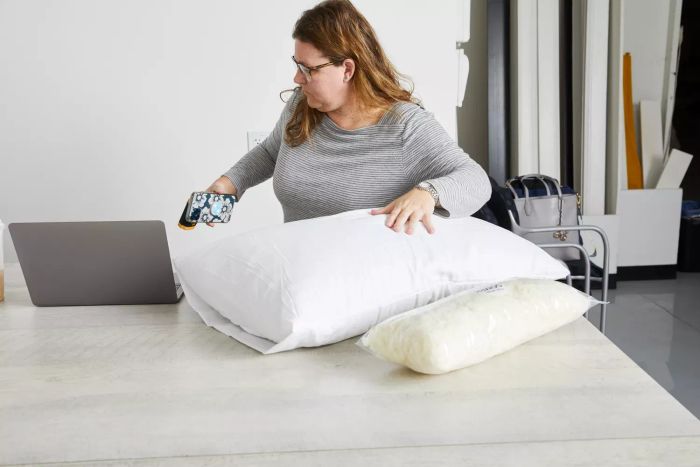 A woman testing the Coop Sleep Goods The Original Pillow on a table beside a laptop