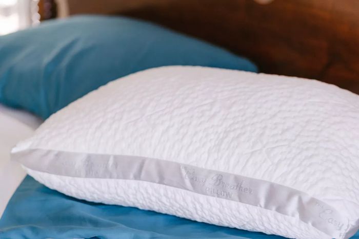 The Nest Bedding Easy Breather Natural Pillow showcased on a bed, with a nearby pillow encased in a pillowcase