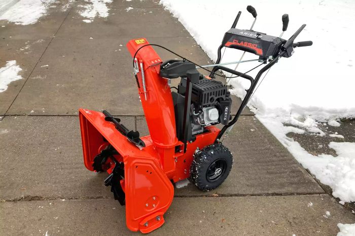 The Ariens Classic 2-Stage 24-Inch Snow Blower is shown on a sidewalk that has been cleared of snow.