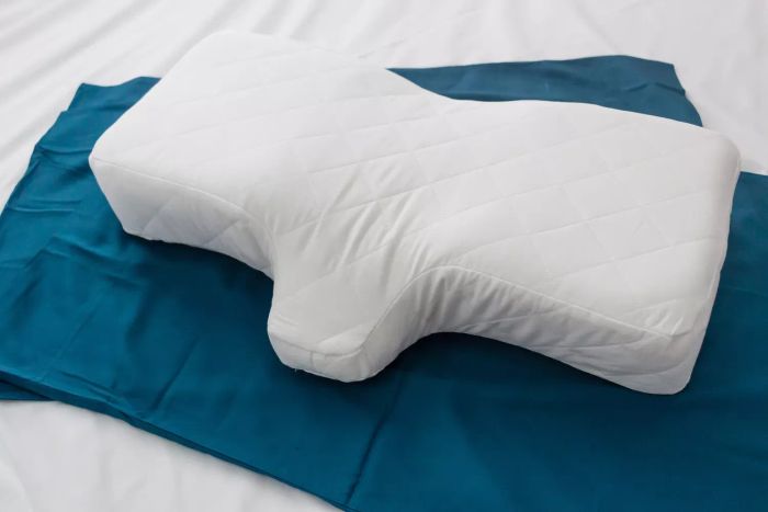 A detailed shot of The Company Store Neck Support Memory Foam Pillow resting on pillowcases atop a bedsheet