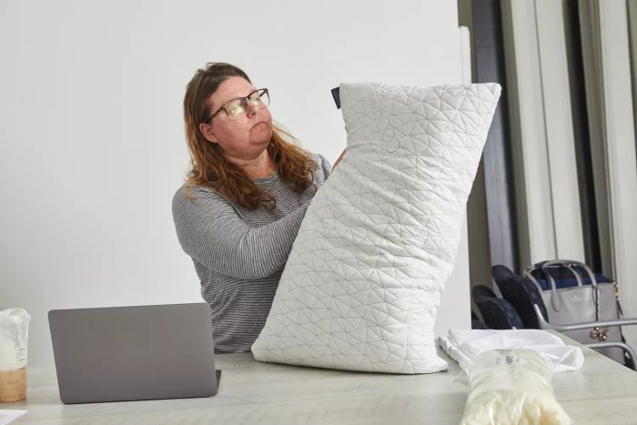 A woman fluffing the Coop Sleep Goods The Original Pillow on a table