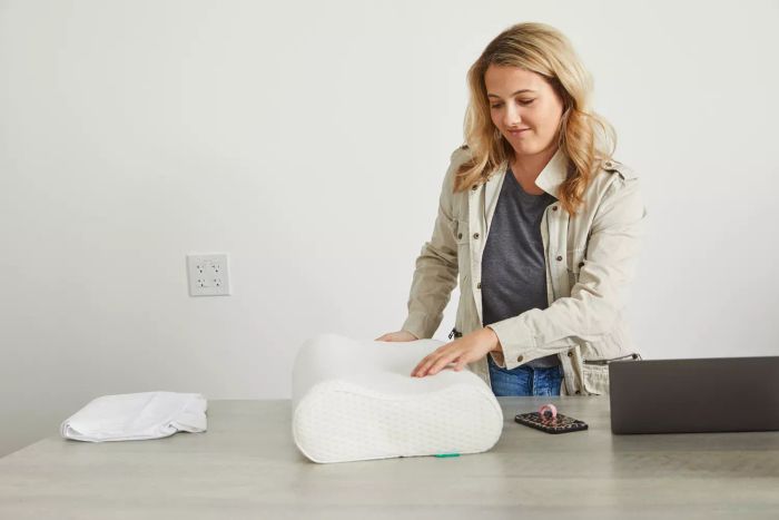 A person touching the Uttu Sandwich Pillow placed on a table beside a laptop