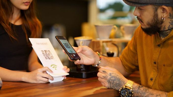 A man scans a QR code on a card held by a woman to complete his coffee payment
