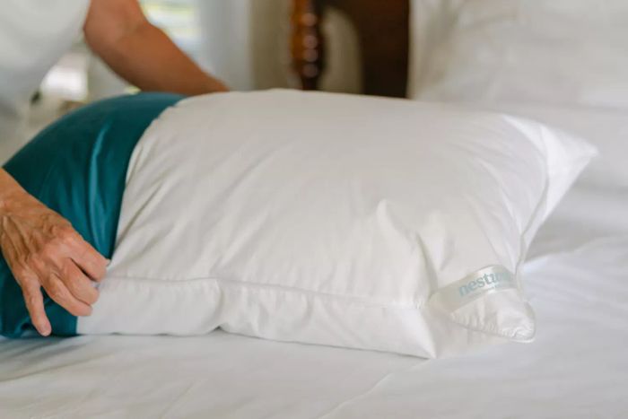 Hands placing a blue pillowcase onto the Nest Bedding Easy Breather Natural Pillow