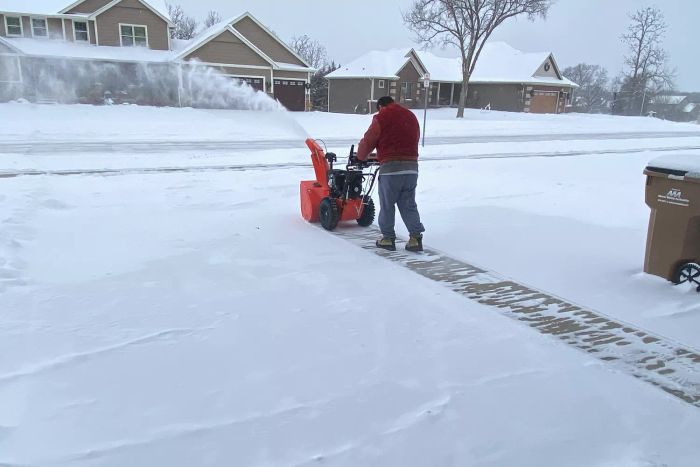 A person using the Ariens Deluxe 28 SHO Snow Blower to clear snow from a driveway