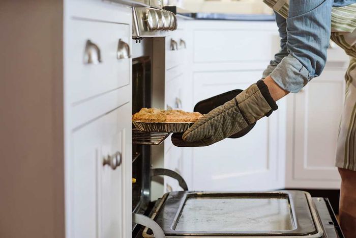 A woman removing a hot pie from the oven.