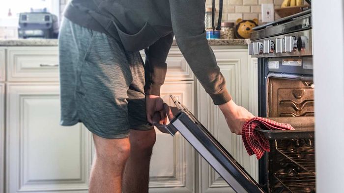 A man removing a baking sheet from the oven using a towel.