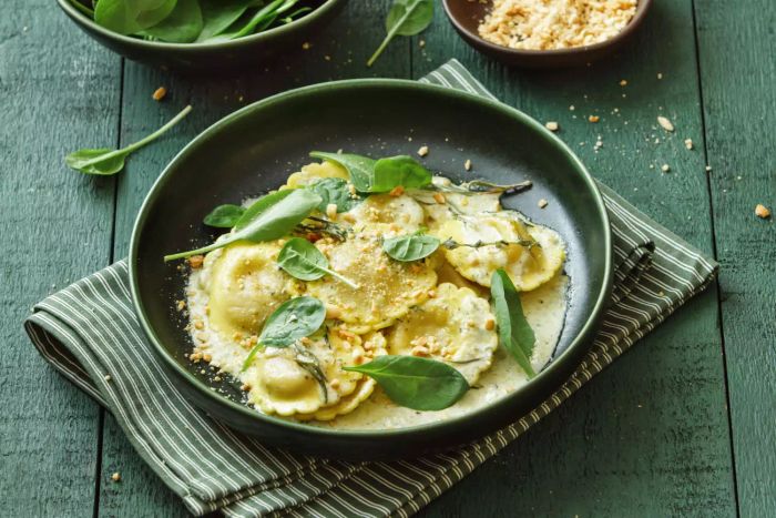 A close-up image of vegan ravioli filled with spinach, wild mushrooms, and walnuts, set against a dark green backdrop.