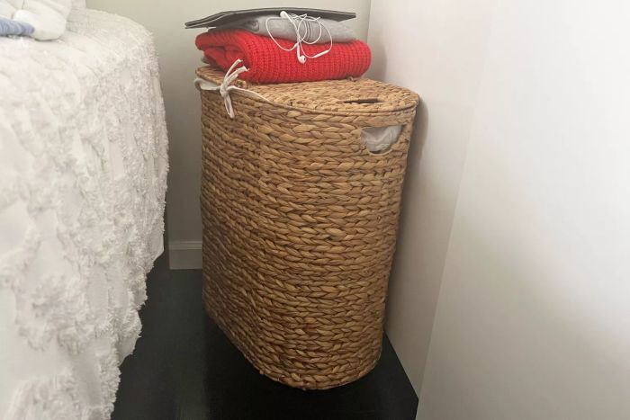 Seville Classics Woven Laundry Hamper sitting in the corner of a room, with clothes piled on top