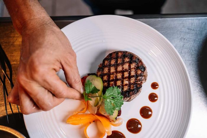 Hand placing garnish on a dish.