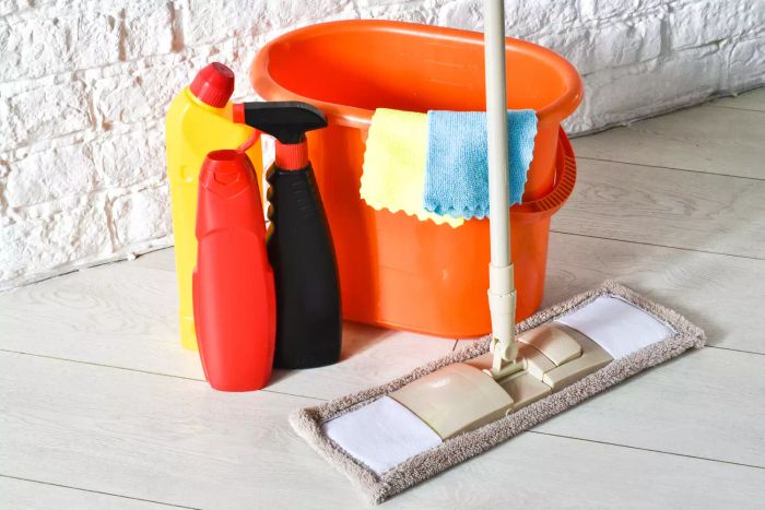 Various cleaning tools and supplies, with an orange mop bucket placed on the floor. Concept of house cleaning service.
