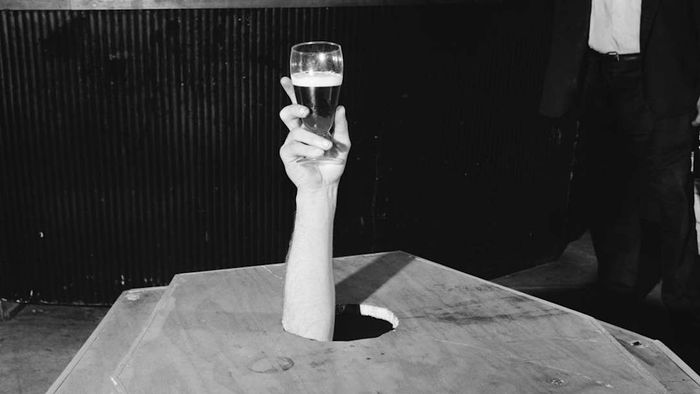 A man holding a beer while lying in a coffin